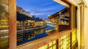 A traditional building with a wooden exterior and a reflection of the river and lights in the window. - Phoenix Ancient City Lingjiang Muyue Riverside Homestay (Fenghuang County)