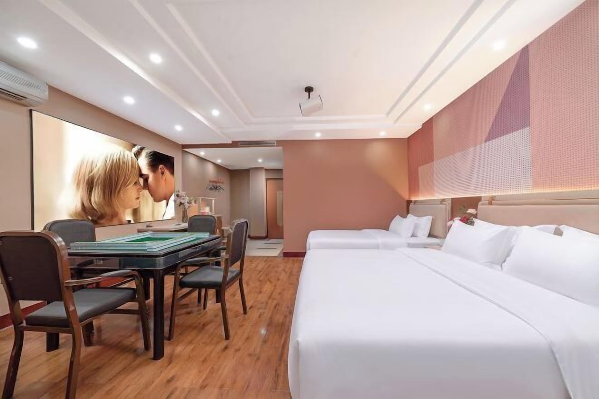 A hotel room with a dining table, chairs, a bed, and a large mirror.