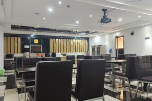 Un salón de conferencias con mesas, sillas, un proyector y una pantalla grande.