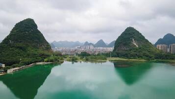 Una superficie acuática tranquila que refleja dos colinas verdes, con un paisaje urbano al fondo.