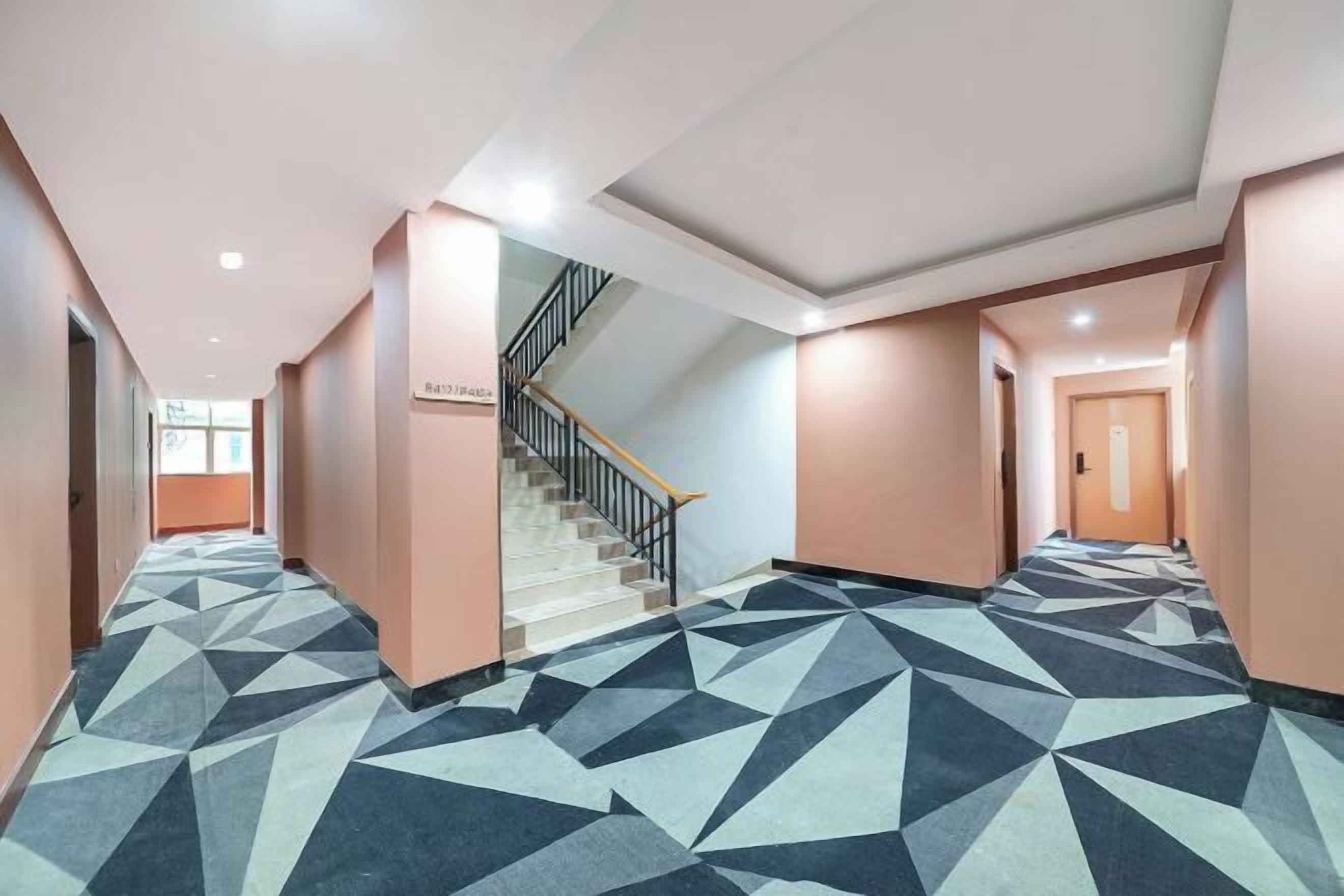 Un pasillo de hotel con una alfombra de diseño geométrico, una escalera y una puerta al final.