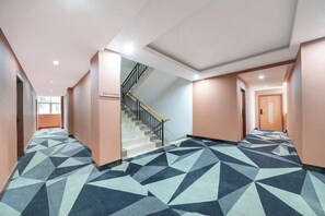 Un pasillo de hotel con una alfombra de diseño geométrico, una escalera y una puerta al final.