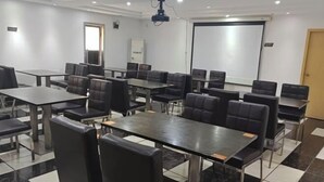 A conference room with multiple tables and chairs, a projector screen, and a whiteboard.