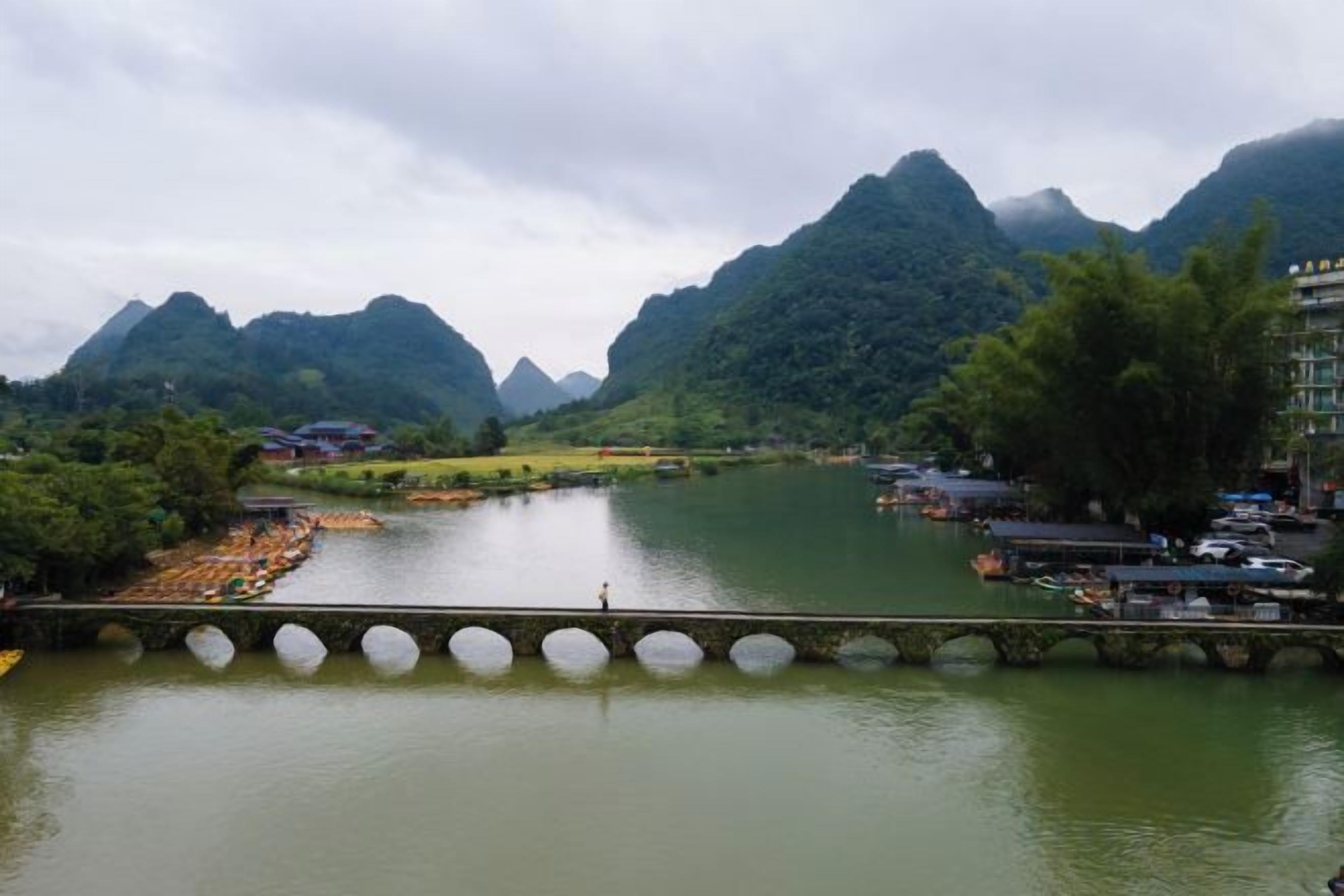 A river with a bridge, mountains in the background, and a building on the right.