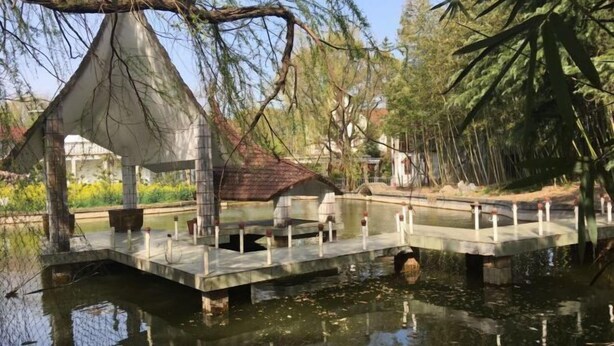 Un puente sobre un estanque con un pabellón y un edificio pequeño al fondo.