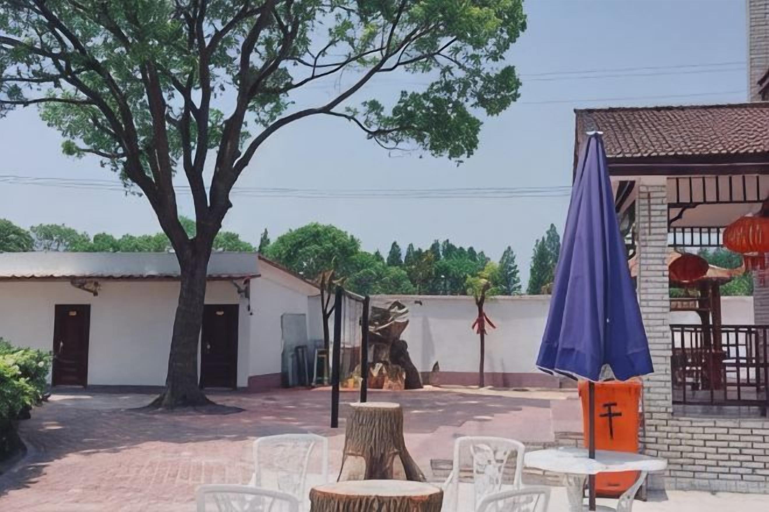 Un patio al aire libre con mesas y sillas, un árbol y un edificio con tejado de baldosas.