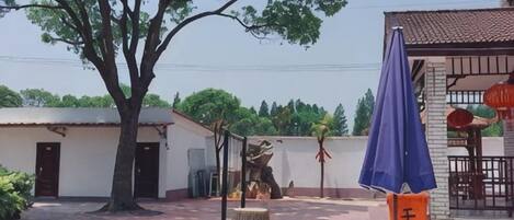 Un patio al aire libre con mesas y sillas, un árbol y un edificio con tejado de baldosas.