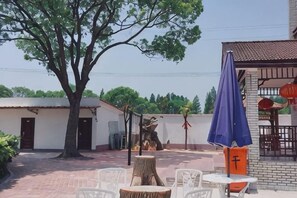 An outdoor patio with tables and chairs, a tree, and a building with a tiled roof. - Beihu Bay Resort (Shanghai)