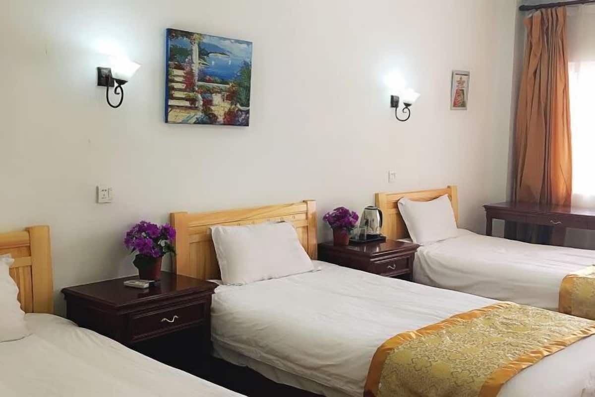 A hotel room with three single beds, wooden headboards, white bedding, a painting on the wall, and wall-mounted lights.