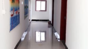 Un pasillo con piso pulido, una ventana con marco morado y una puerta a la derecha.