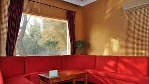 Un sofá rojo con una mesa de madera al frente, una ventana con cortinas y una pared con textura.