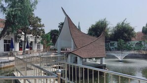 Un edificio moderno con una estructura de techo triangular distintiva, una fuente de agua y una barandilla metálica con vista a un cuerpo de agua.