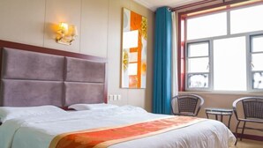 A hotel room with a large bed, a headboard, a wall-mounted light fixture, a window with curtains, and two chairs. - Jingbian Danxia Tourism Resort (Jingbian County)