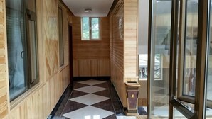 A hallway with wooden walls, a checkered floor, and large windows. - Niegan Dawa Hotel (Diebu)