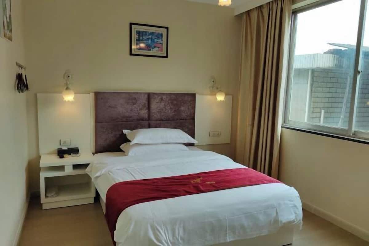 A hotel room with a bed, a nightstand, a window with curtains, and a painting on the wall.