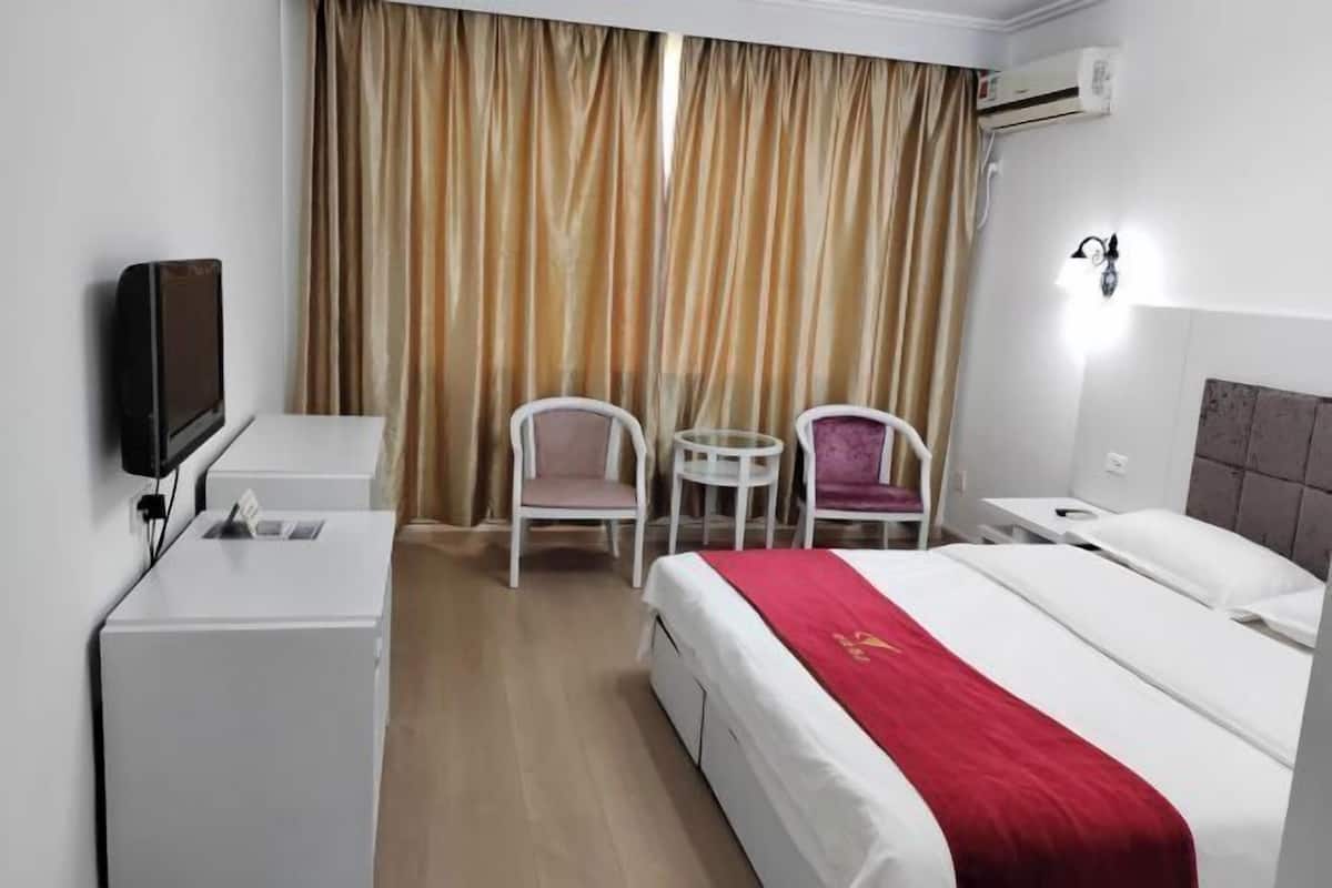 A hotel room with a bed, a desk, a chair, a small table, and a TV.