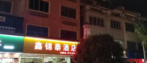 A building with a brightly lit sign, a storefront with a visible entrance, and a tree in front.