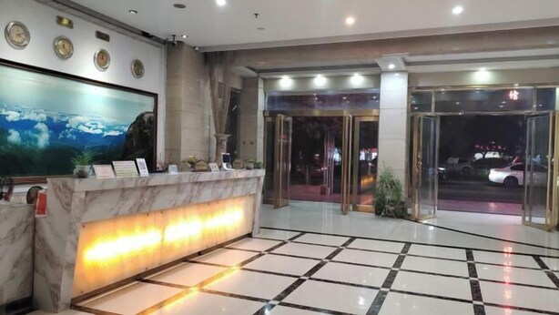 A hotel reception area with a marble counter, a large painting, and a glass door entrance. - Xinjingtai Hotel Xing'an (Xing'an County)