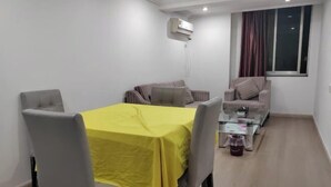 A dining area with a yellow table, grey chairs, a glass coffee table, and a sofa with cushions. - Xinjingtai Hotel Xing'an (Xing'an County)