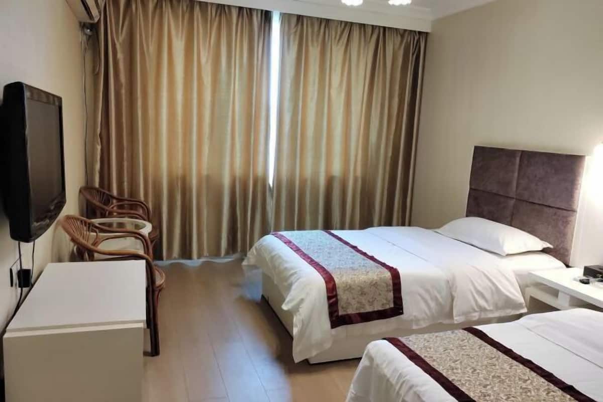 A hotel room with two beds, a TV, a desk, and a chair.