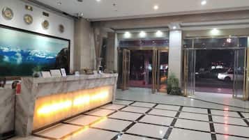 A hotel reception area with a marble counter, a large painting, and a glass door entrance.