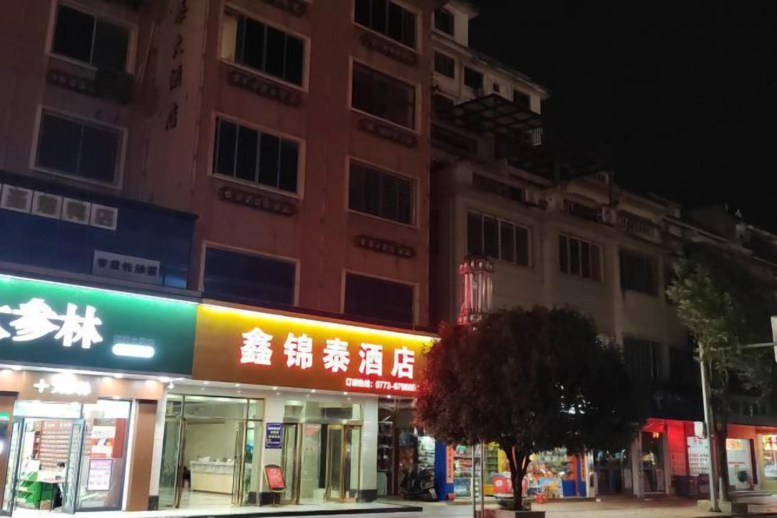 A building with multiple storefronts, including a brightly lit restaurant and a pharmacy.