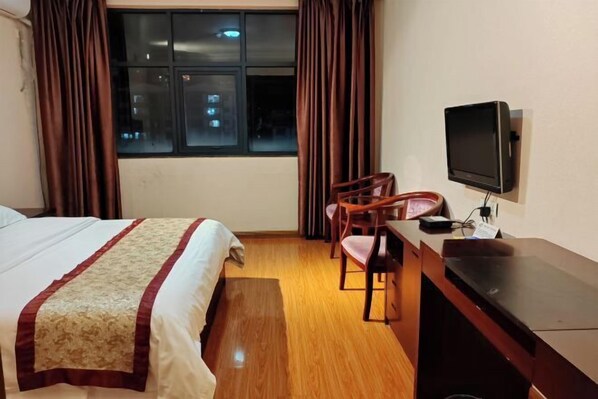 A hotel room with a bed, a desk with a television, and a window with curtains.