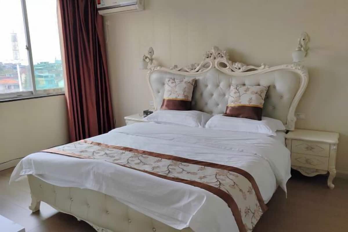 A bedroom with a large bed, a nightstand, and a window with curtains.