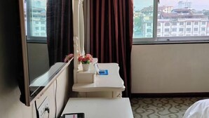 A hotel room with a bed, a bedside table with a phone, a mirror, a window with curtains, and a view of buildings. - Xinjingtai Hotel Xing'an (Xing'an County)