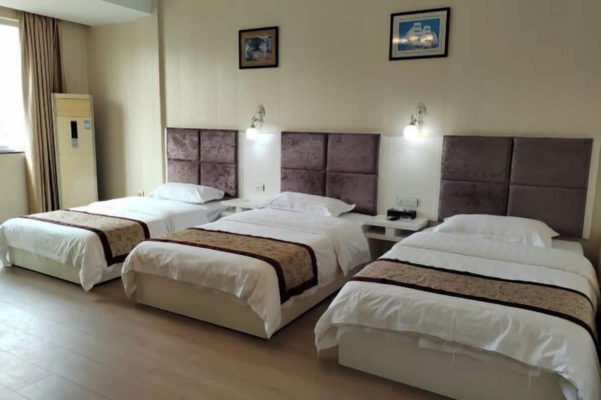 A hotel room with three beds, each with a headboard and bedside tables.