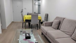 A living room with a glass coffee table, a sofa, a dining table with chairs, and a door. - Xinjingtai Hotel Xing'an (Xing'an County)