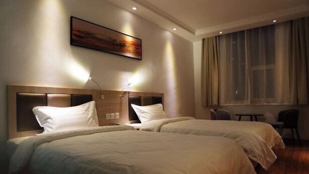 Ein Hotelzimmer mit zwei Betten, einem Bild an der Wand und einem Fenster mit Vorhängen.