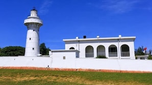 A lighthouse with a white exterior, a building with arched windows, and a clear blue sky. - Kenting Hostel（Villa） (Pingtung)