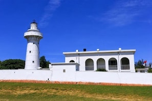 A lighthouse with a white exterior, a building with arched windows, and a clear blue sky. - Kenting Hostel（Villa） (Pingtung)