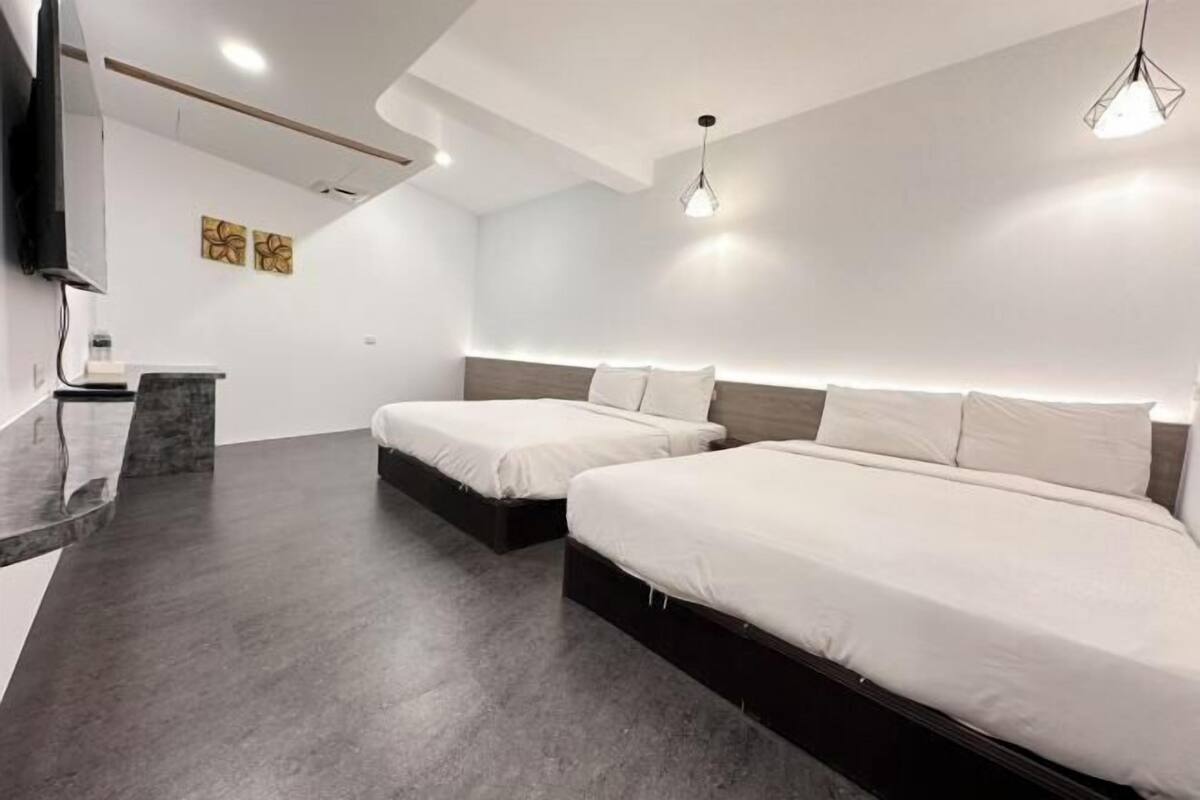A modern hotel room with two beds, a flat-screen TV, and a small desk with a mirror.