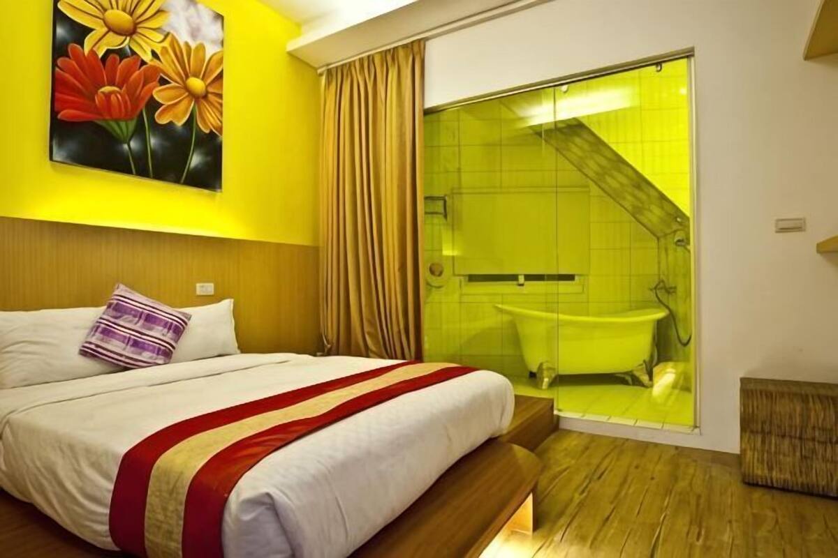 Une chambre d’hôtel avec un lit, un tableau, une salle de bain dont un mur est recouvert de carreaux jaunes, et un plancher en bois.