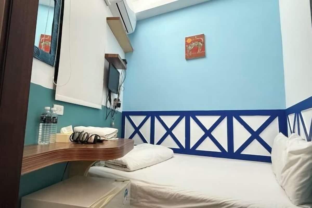 A hotel room with a bed, a desk with a telephone, a mirror, and a wall-mounted air conditioner.