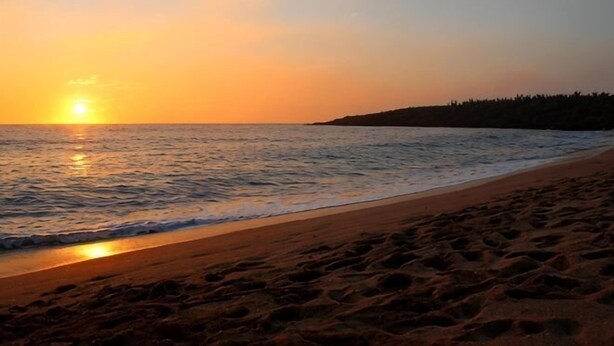 A beach with footprints leading to the water, a sunset in the background, and a tree line on the right. - Kenting Hostel（Villa） (Pingtung)