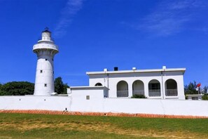A lighthouse with a white exterior, a building with arched windows, and a clear blue sky. - Kenting Hostel（Villa） (Pingtung)