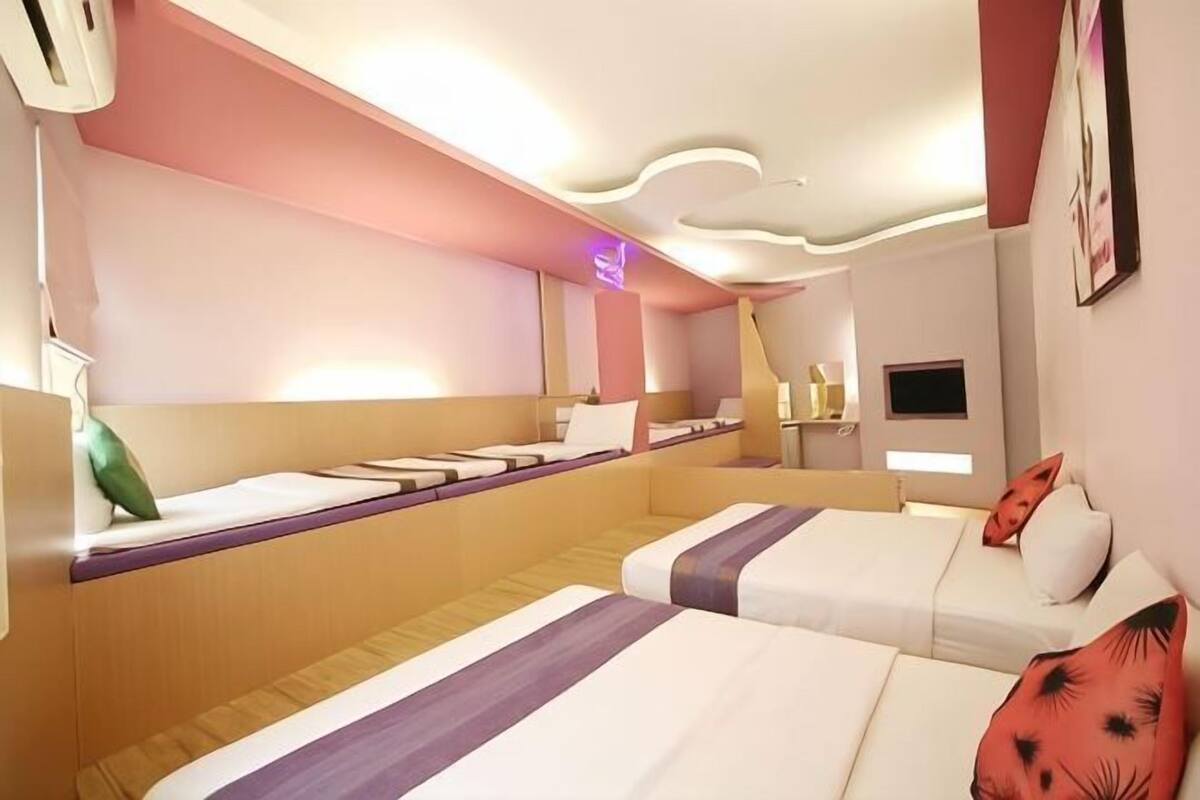 A hotel room with two beds, a small desk, a TV, and a wall-mounted air conditioner.