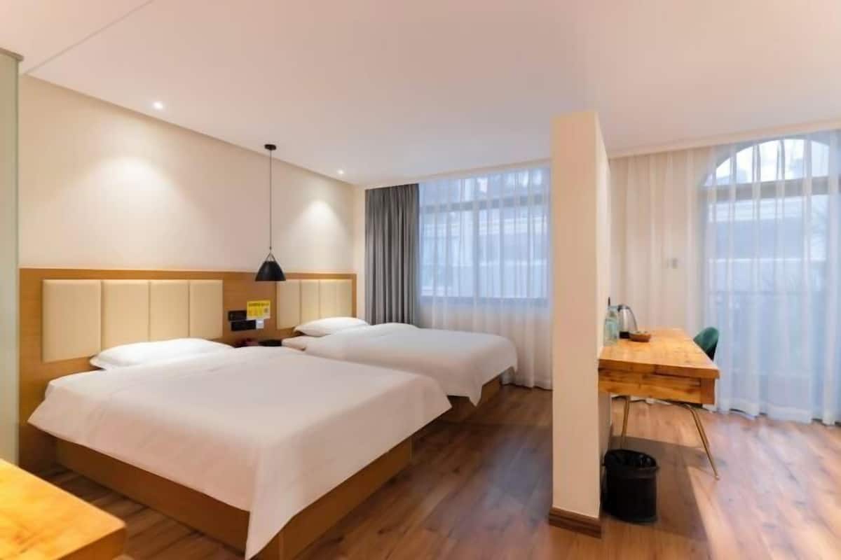 A hotel room with two beds, a desk, a chair, a lamp, and a window with curtains.