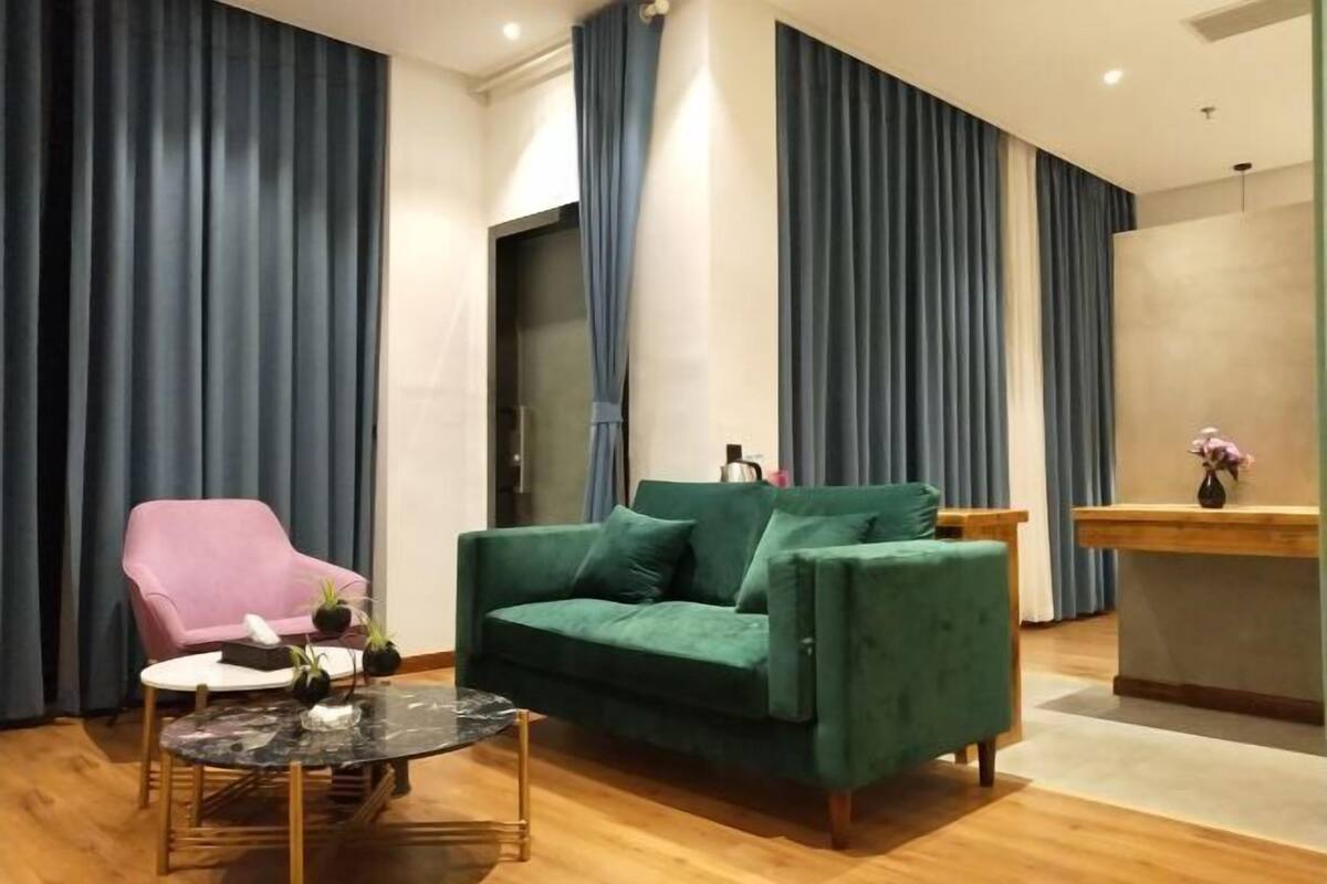 A living room with a green sofa, a pink chair, a glass coffee table, and a wooden side table.