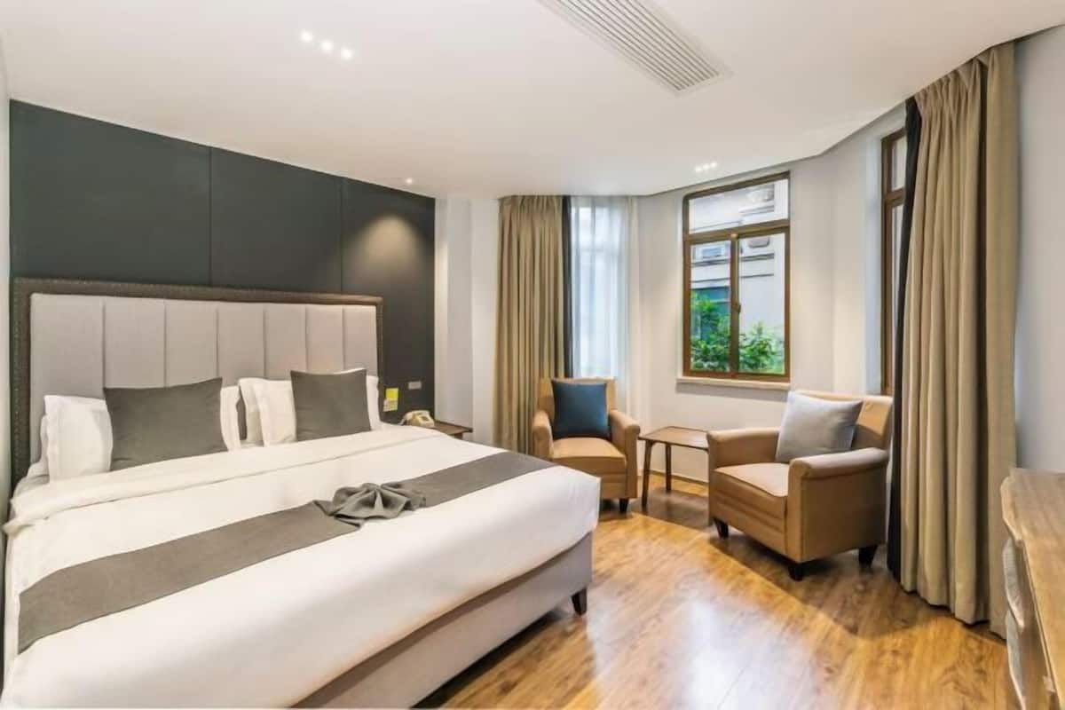 A hotel room with a large bed, two armchairs, a small table, and a window with curtains.