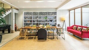 Un salon moderne comprenant un coin repas, un canapé rouge et une étagère murale où sont exposés divers objets.