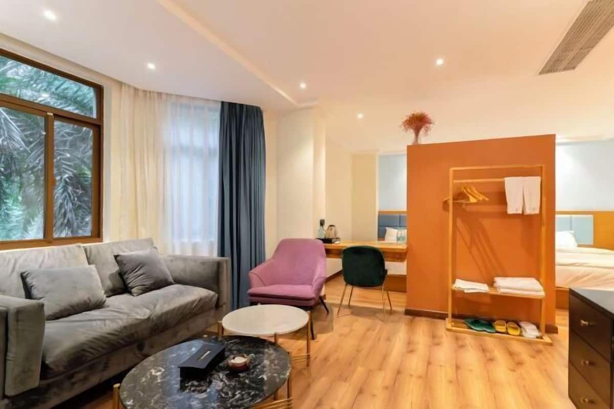 A hotel room with a sofa, a small round table, a chair, a bed, a wardrobe, and a desk with a chair.