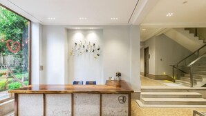 Un espace d’accueil avec un comptoir de réception en bois, une œuvre d’art accrochée au mur et un escalier menant à un niveau supérieur.