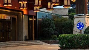 A hotel entrance with a modern design, featuring a stone pathway leading to the entrance, a blue circular sign with arrows, and a well-maintained garden area. - Jade Jianguo Resort Zhejiang Pan'an (Pan'an)