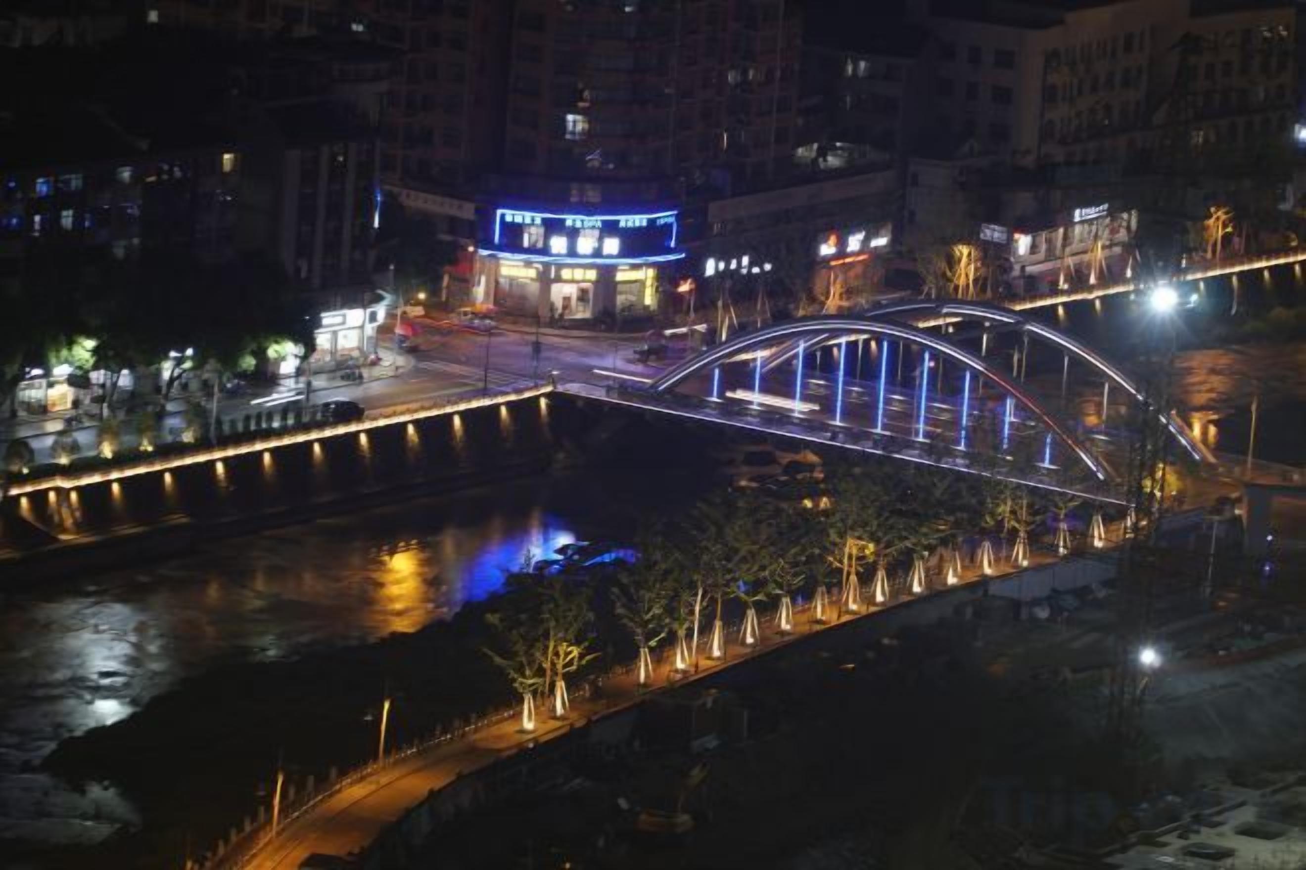 A nighttime view of a bridge with illuminated railings and a lit-up building in the background.