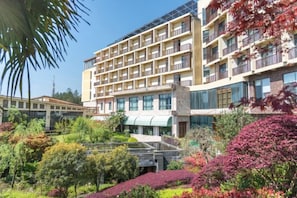 Un hotel de varios pisos con un diseño moderno, con balcones en cada planta, rodeado de jardines ajardinados y un cielo despejado.
