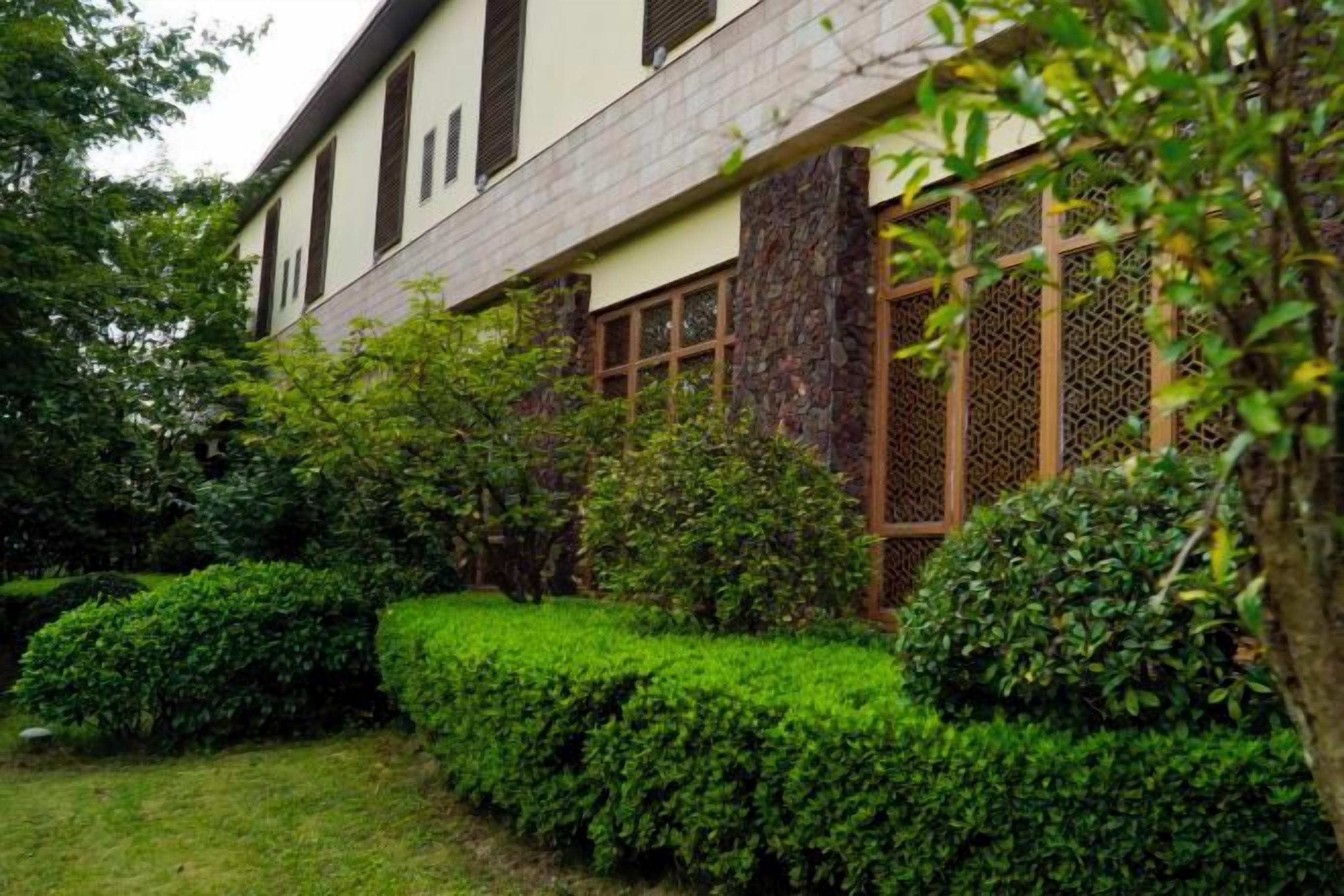 Un edificio tradicional con tejado de tejas, marcos de ventana de madera y un jardín bien cuidado con arbustos podados.